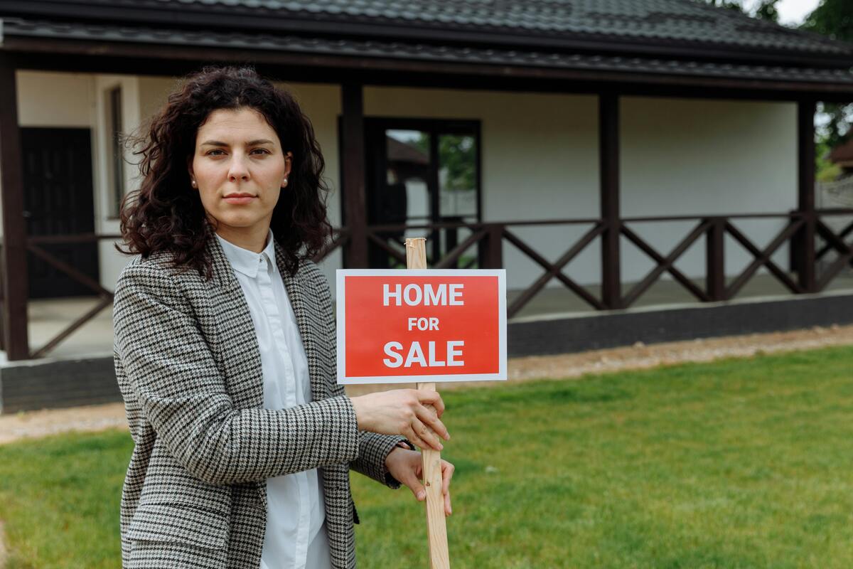 A woman holding a home for sale signage