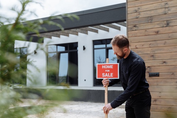 A man putting a for sale sign in front of his house