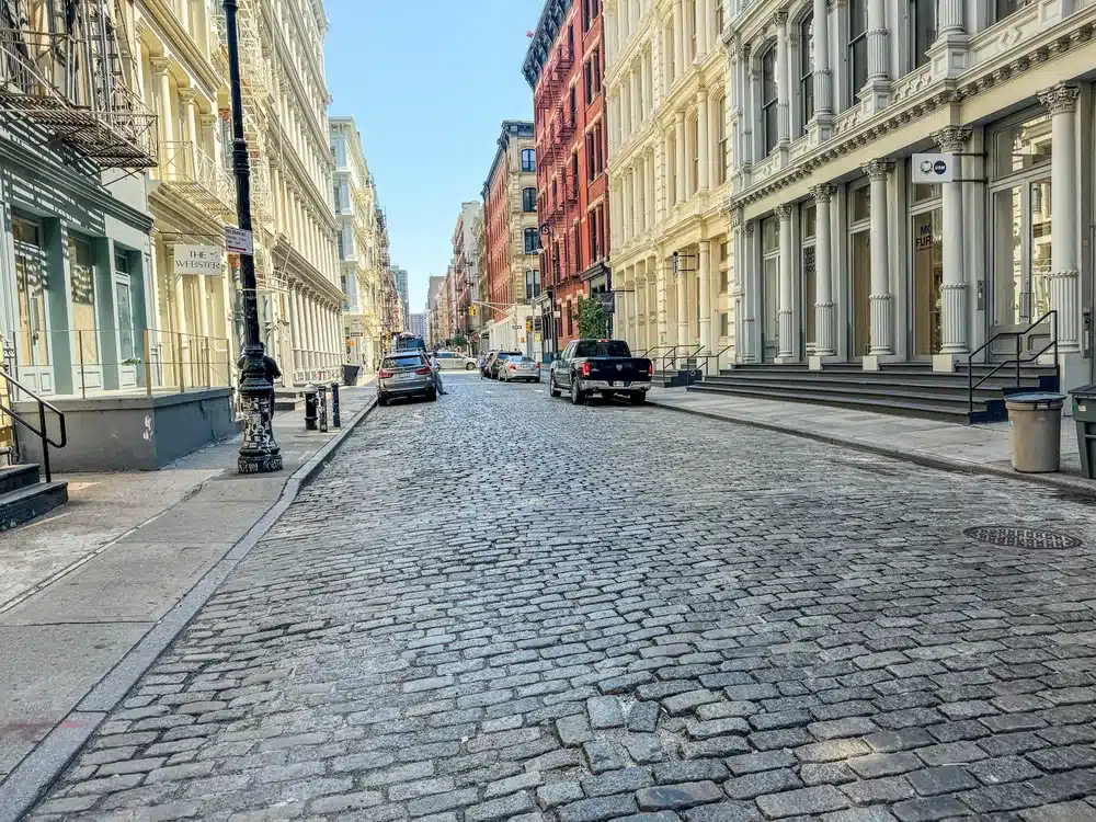 Greene Street in SoHo, New York City, featuring historic cast-iron buildings and cobblestone street.